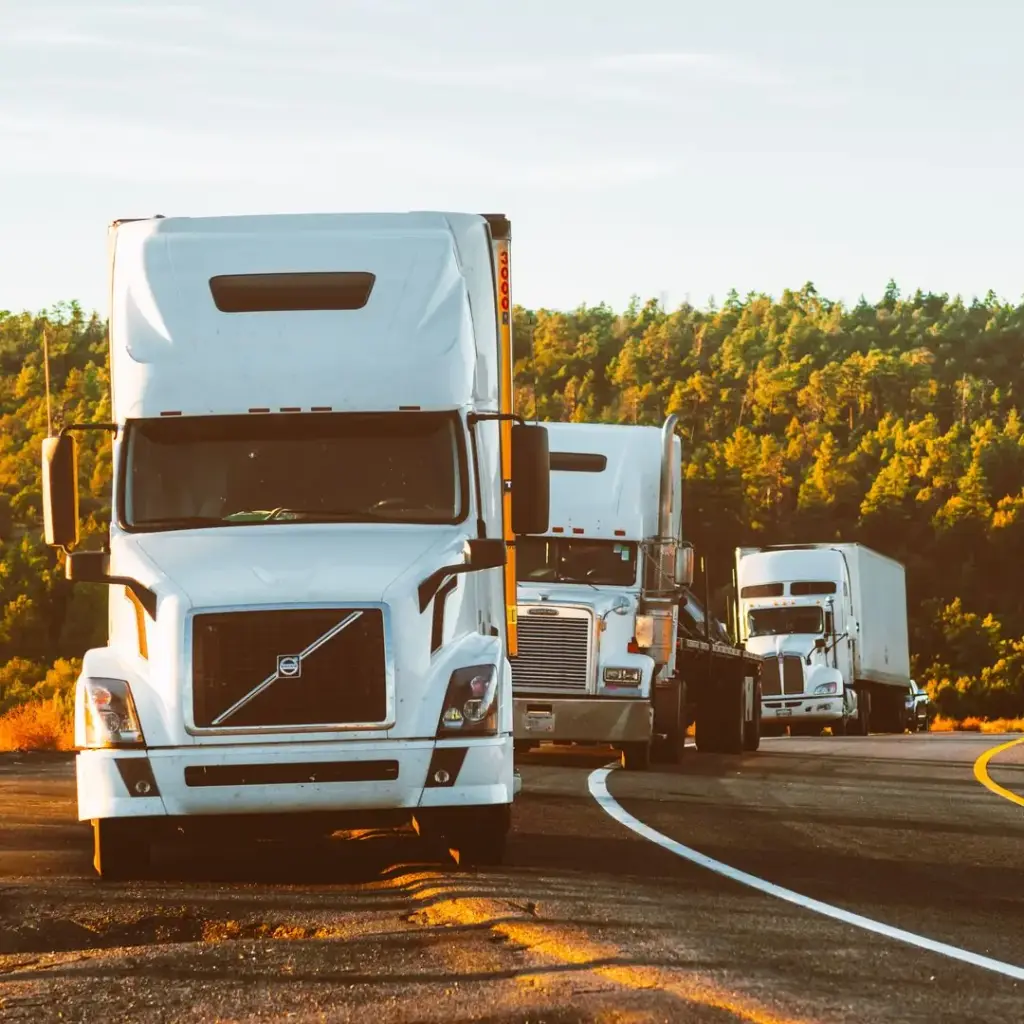 Three white Volvo semi trucks driving on a highway at sunset, representing the best CB radios for truckers in 2026